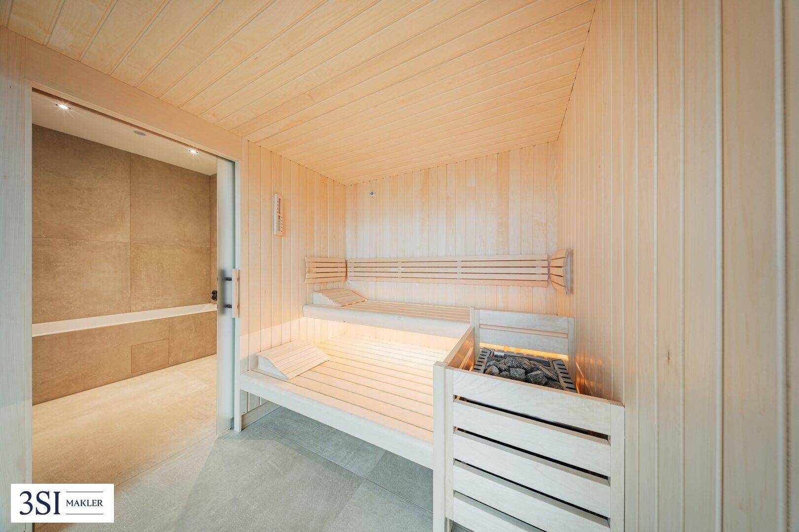 Helle Holzsauna mit Bänken und Saunaofen, direkt an ein modernes Badezimmer angrenzend.