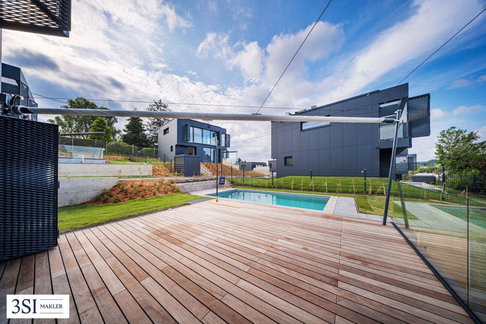 Außenbereich mit Holzterrasse, kleinem Pool und Blick auf moderne Gebäude in grüner Umgebung.