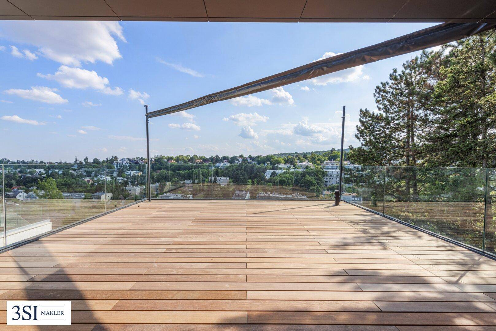 Geräumige Holzterrasse mit Markise und weitem Blick auf die umliegende Natur und Siedlung.