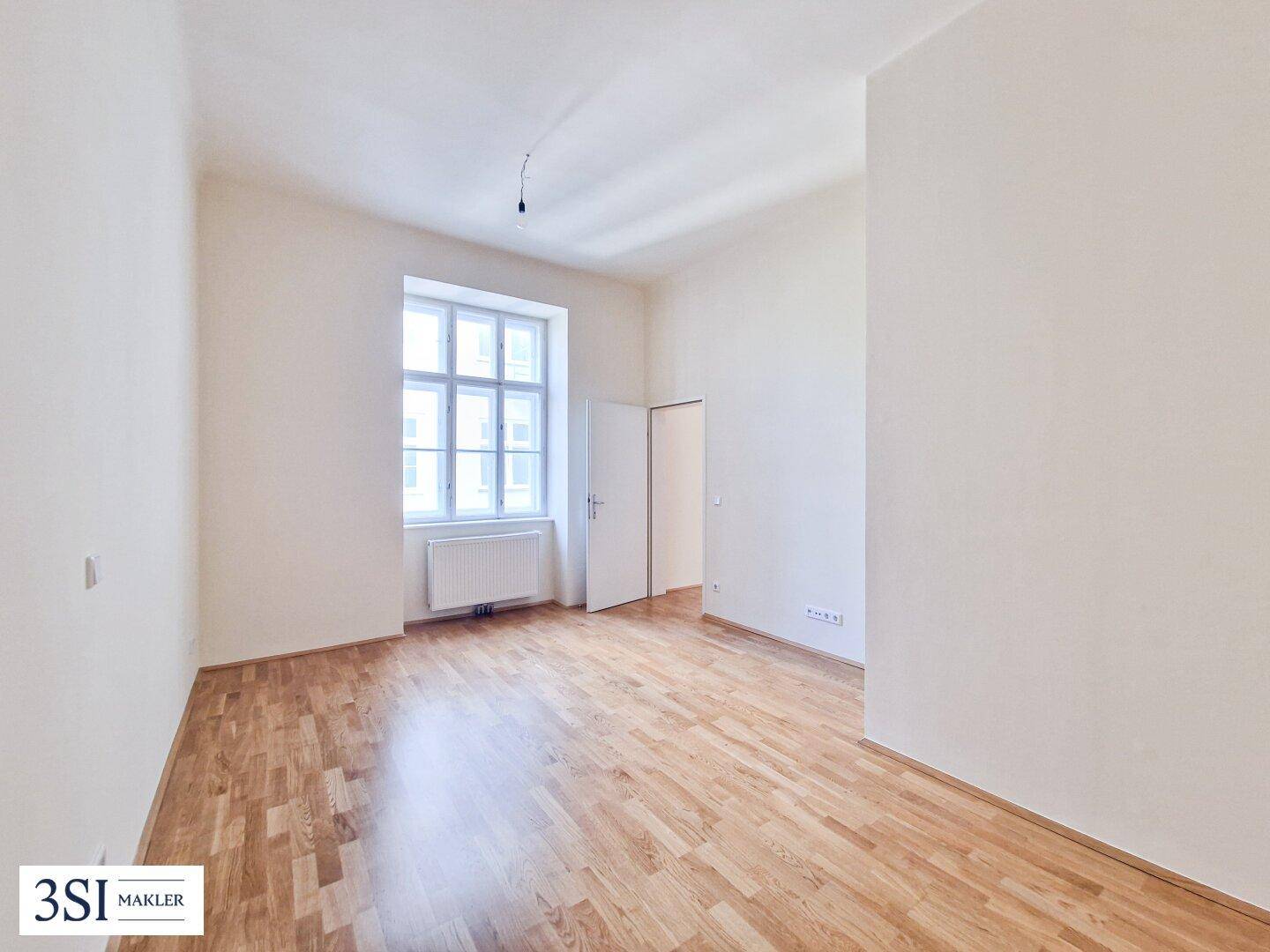Heller Raum mit Parkettboden und einem großen Fenster, ideal als Wohn- oder Schlafzimmer nutzbar.