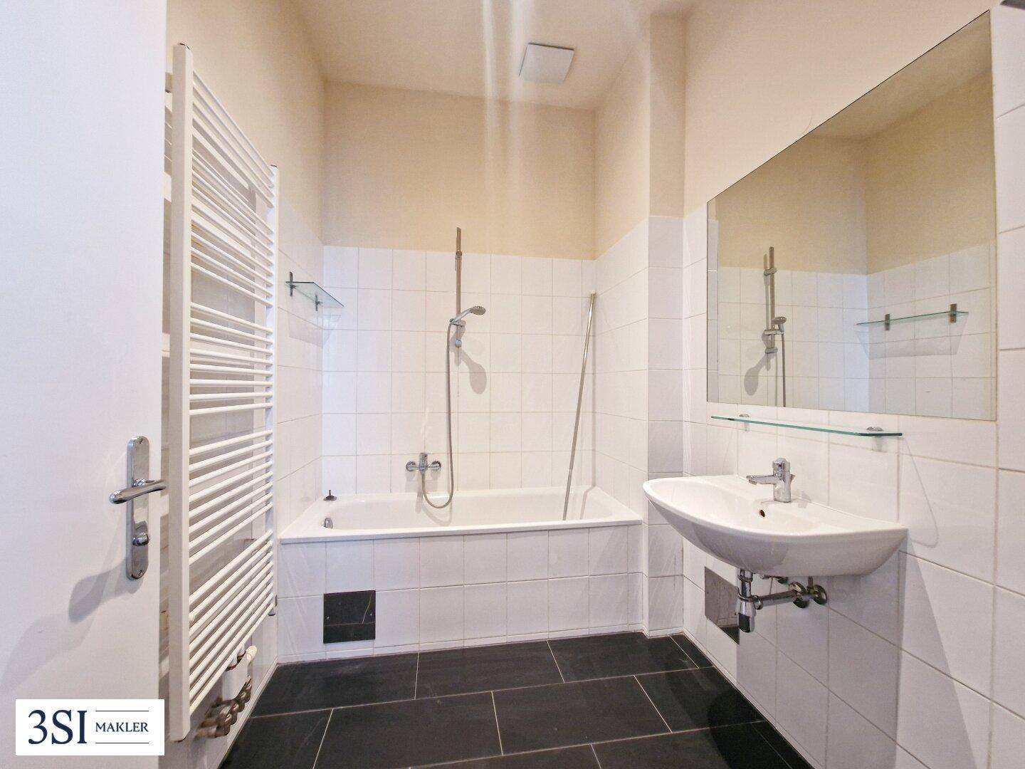 Badezimmer mit Badewanne, Duschfunktion, Waschbecken und beheiztem Handtuchhalter in weißer Fliesenoptik.