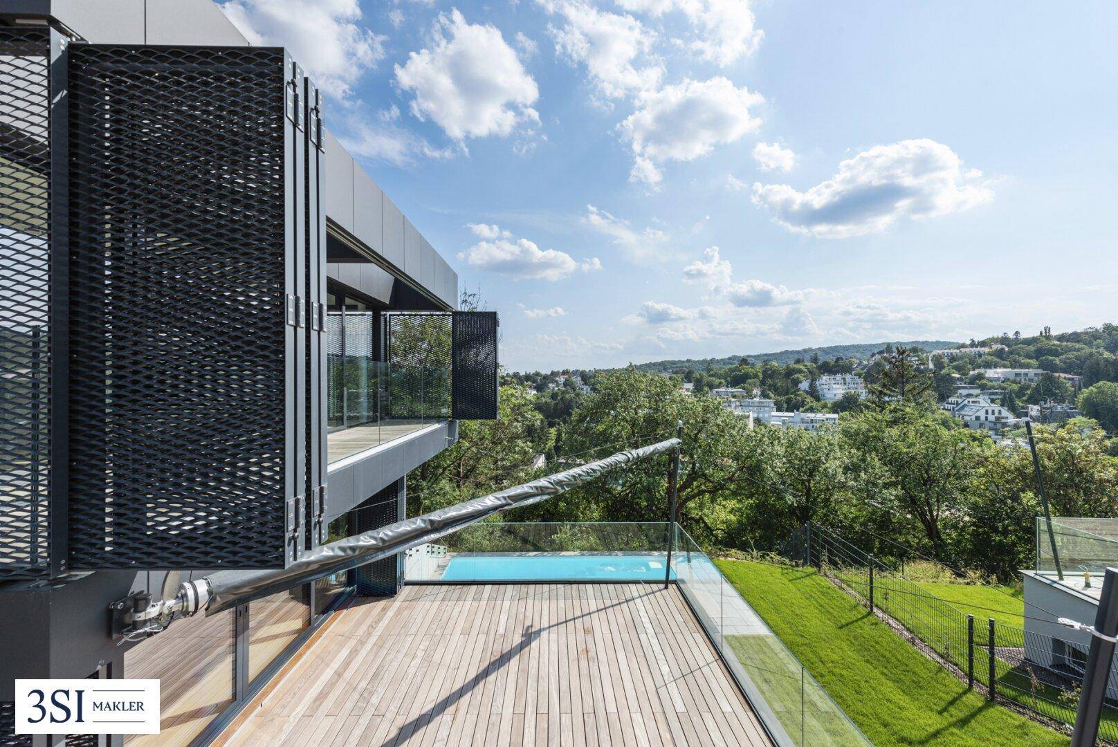 Große Holzterrasse mit Glasgeländer und Blick auf den Pool sowie die weite Landschaft.