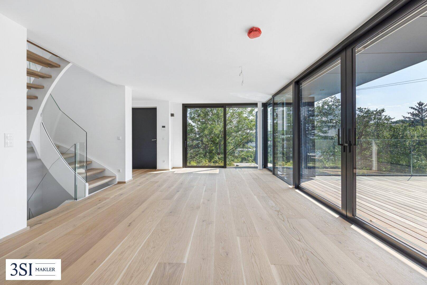 Geräumiger Wohnbereich mit elegantem Holzparkett, moderner Treppe und Zugang zur Außenterrasse.