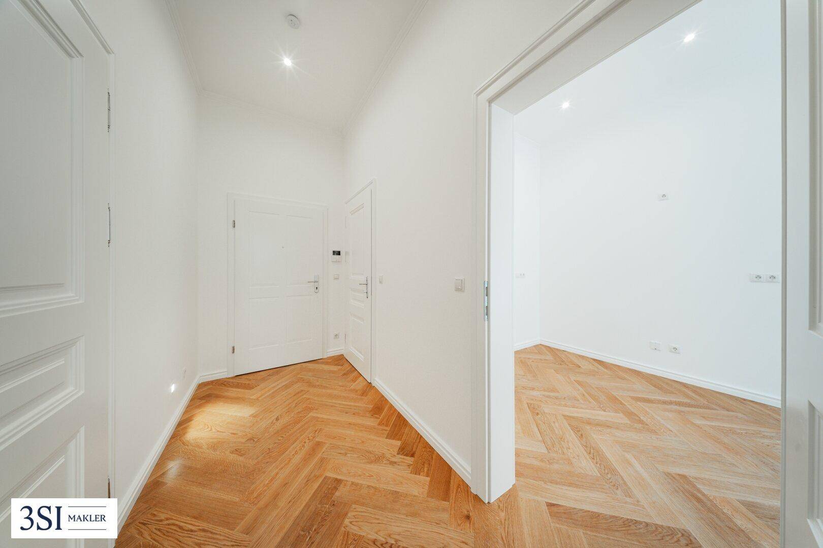 Heller Flur mit elegantem Fischgrätparkett und weißen Türen, der zu den verschiedenen Räumen führt.
