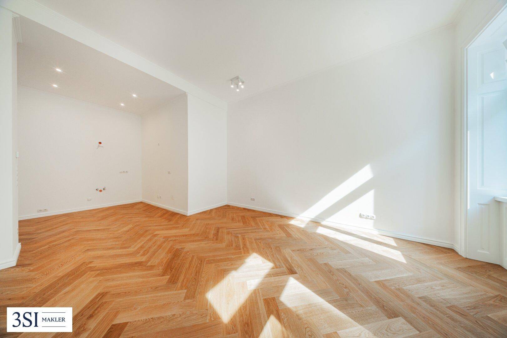 Geräumiger, heller Raum mit Fischgrätparkett und viel Tageslicht, ideal für offenes Wohnen.