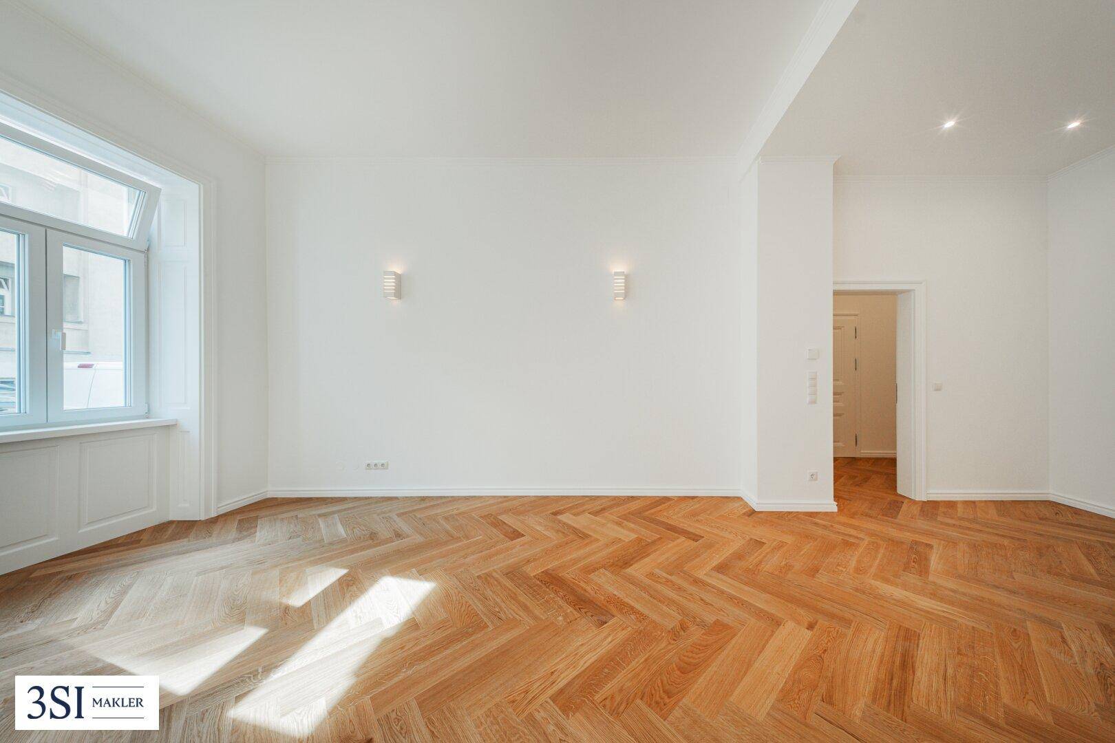 Geräumiges Wohnzimmer mit hellem Fischgrätparkett und modernen Wandleuchten, bereit zur individuellen Gestaltung.