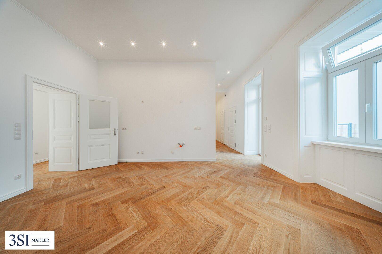 Geräumiges Zimmer mit elegantem Fischgrätparkett und Zugang zu weiteren Räumen.