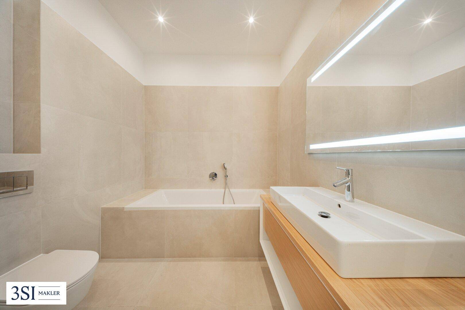 Modernes Badezimmer mit integrierter Badewanne, elegantem Waschtisch und beleuchtetem Spiegel.