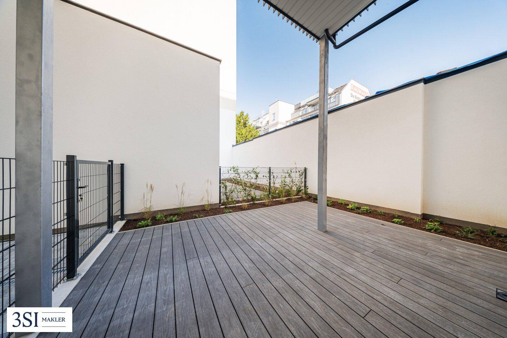 Moderne Terrasse mit Holzdecking und kleiner Grünfläche, umgeben von hohen Mauern.