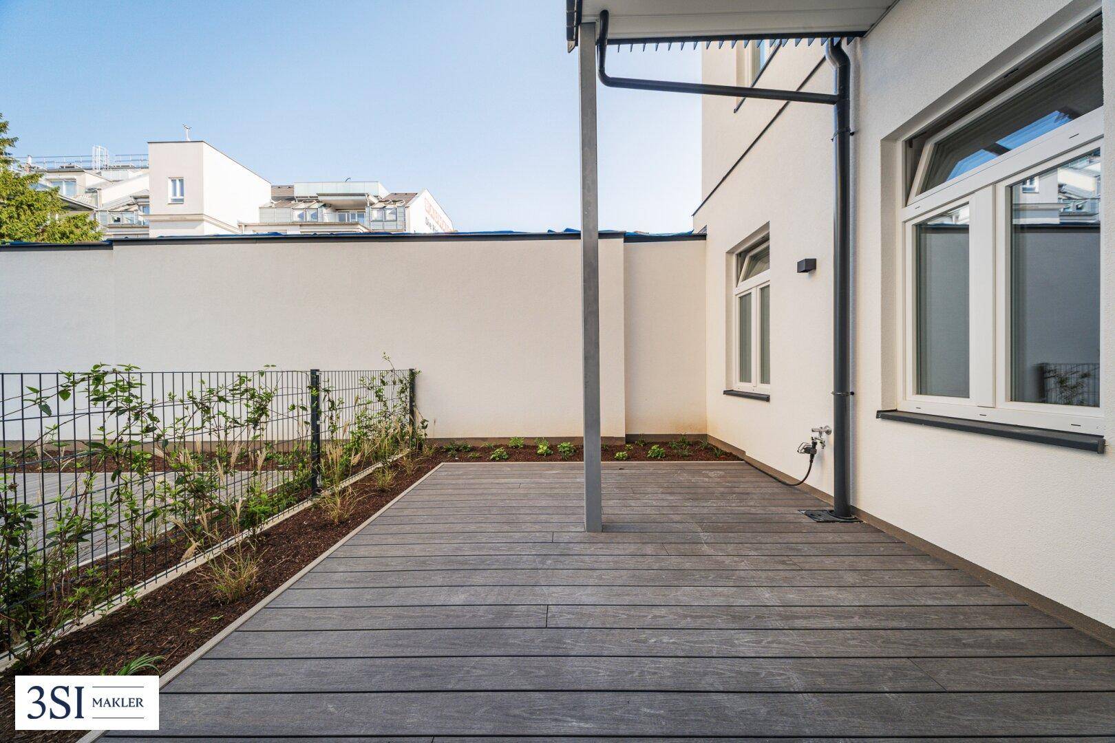 Geräumige Terrasse mit Holzdecking und Blick auf die moderne Gebäudefassade.