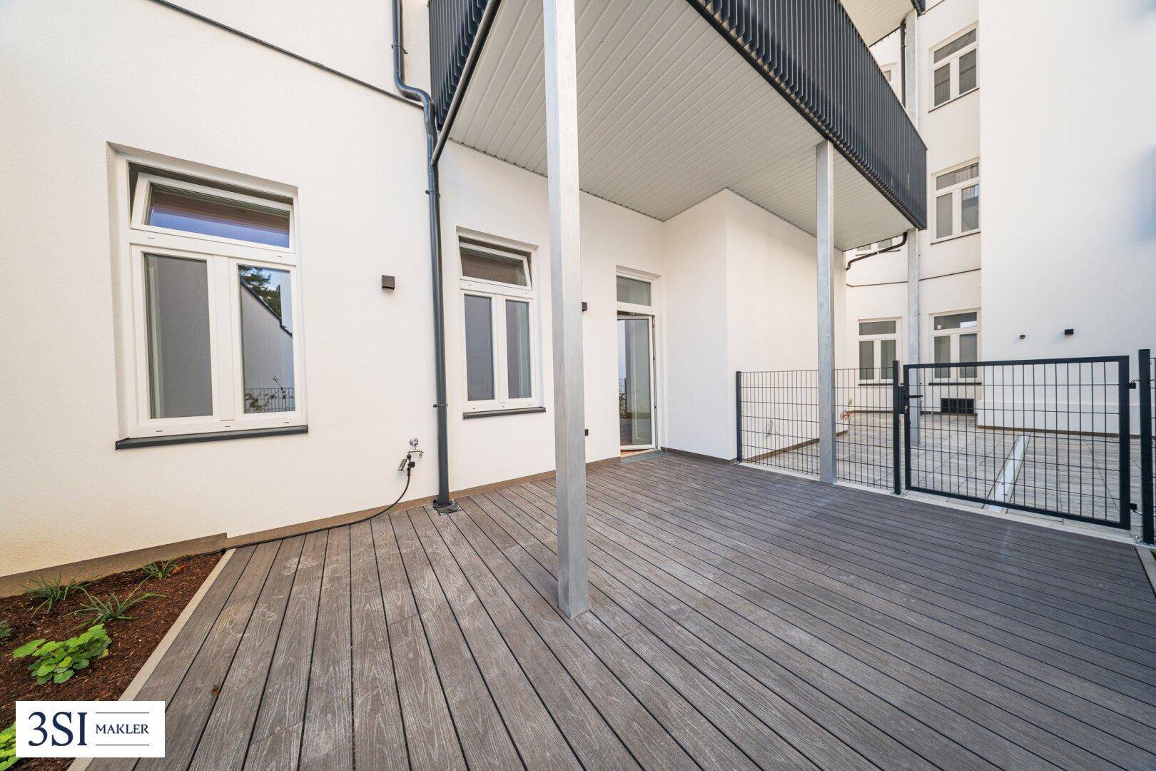 Große Terrasse mit Holzdecking und Blick auf die Gebäudefassade und einen oberen Balkon.