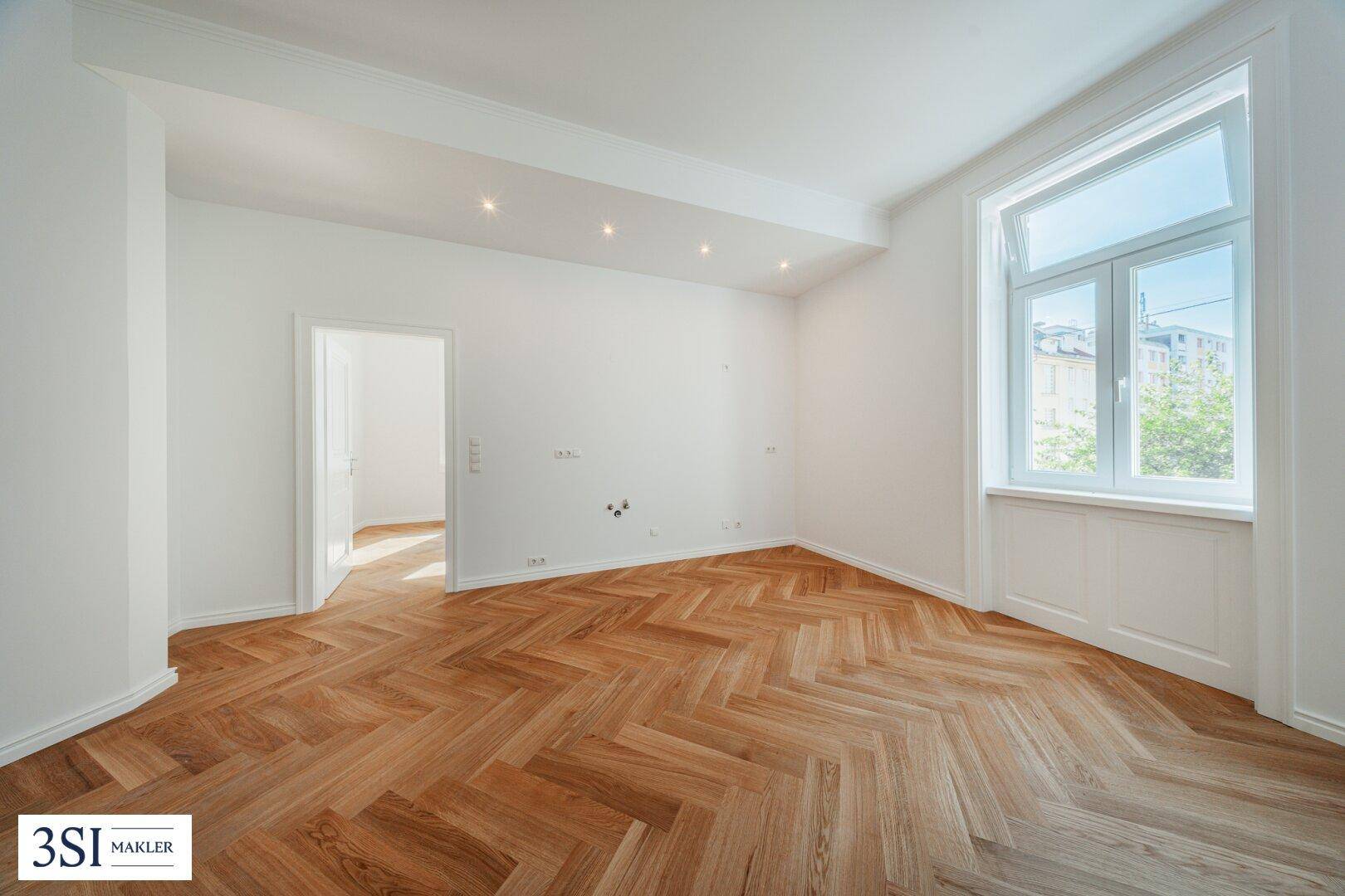 Geräumiger, heller Raum mit Fischgrätparkett und großen Fenstern, ideal für ein Wohn- oder Schlafzimmer.