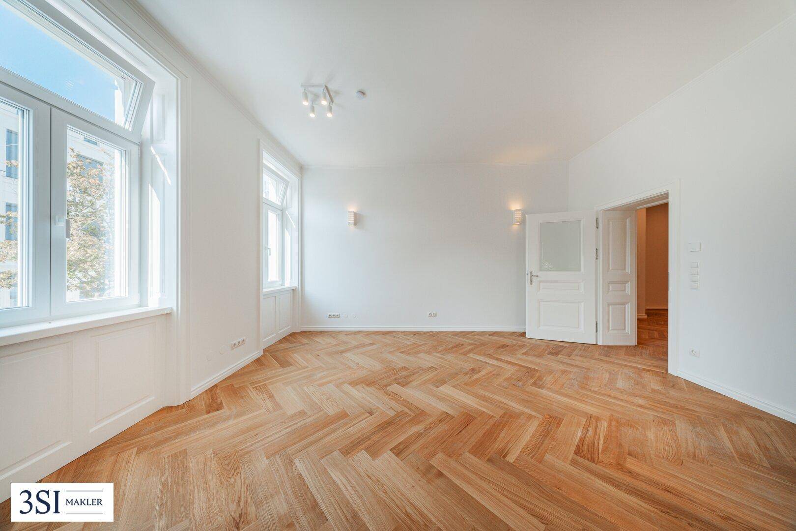 Heller Raum mit Fischgrätparkett und hohen Fenstern, der vielseitig als Wohn- oder Schlafzimmer genutzt werden kann.