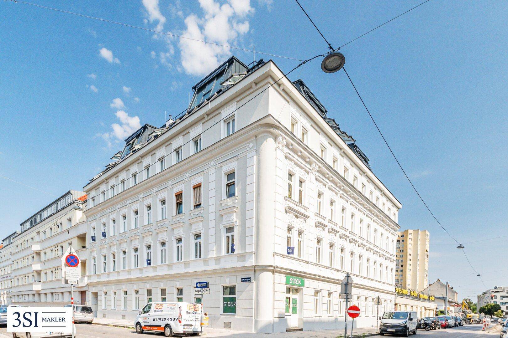 Historisches Eckgebäude mit eleganter Fassade und vielen Fenstern unter blauem Himmel.