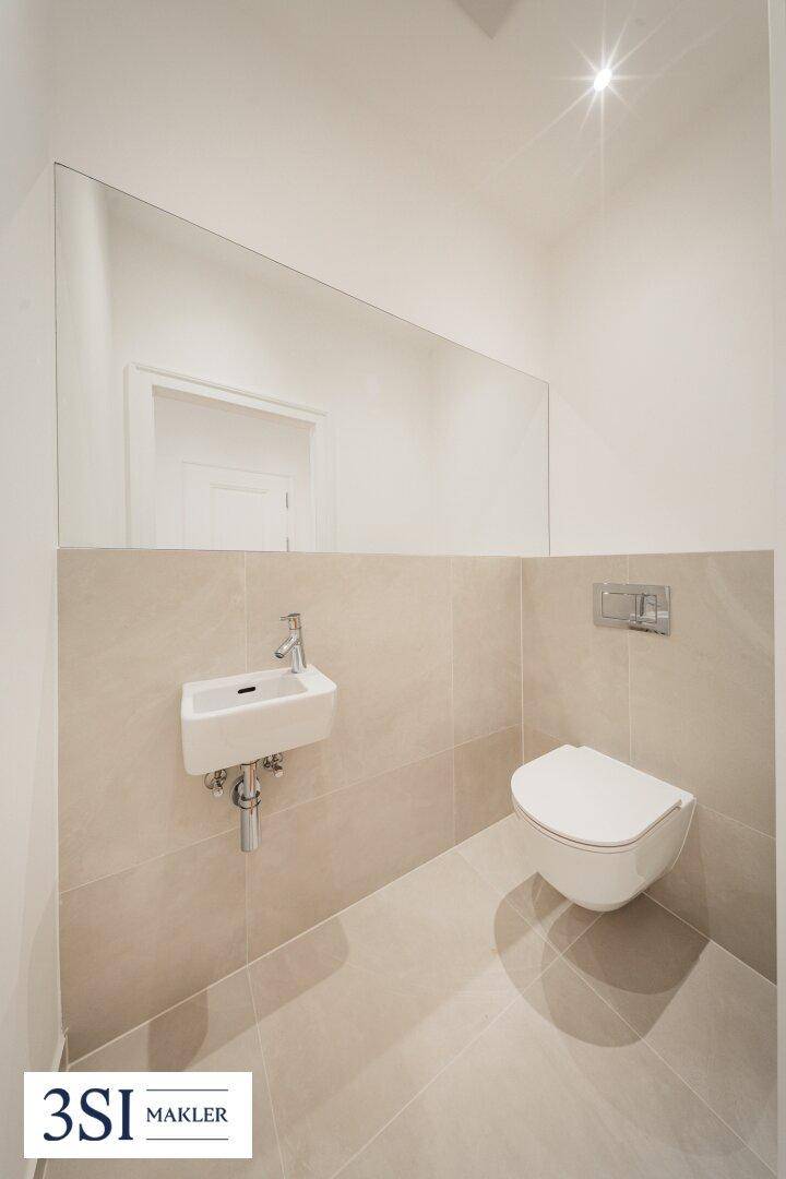 Modernes Gäste-WC mit wandhängender Toilette, kleinem Waschbecken und großem Spiegel.