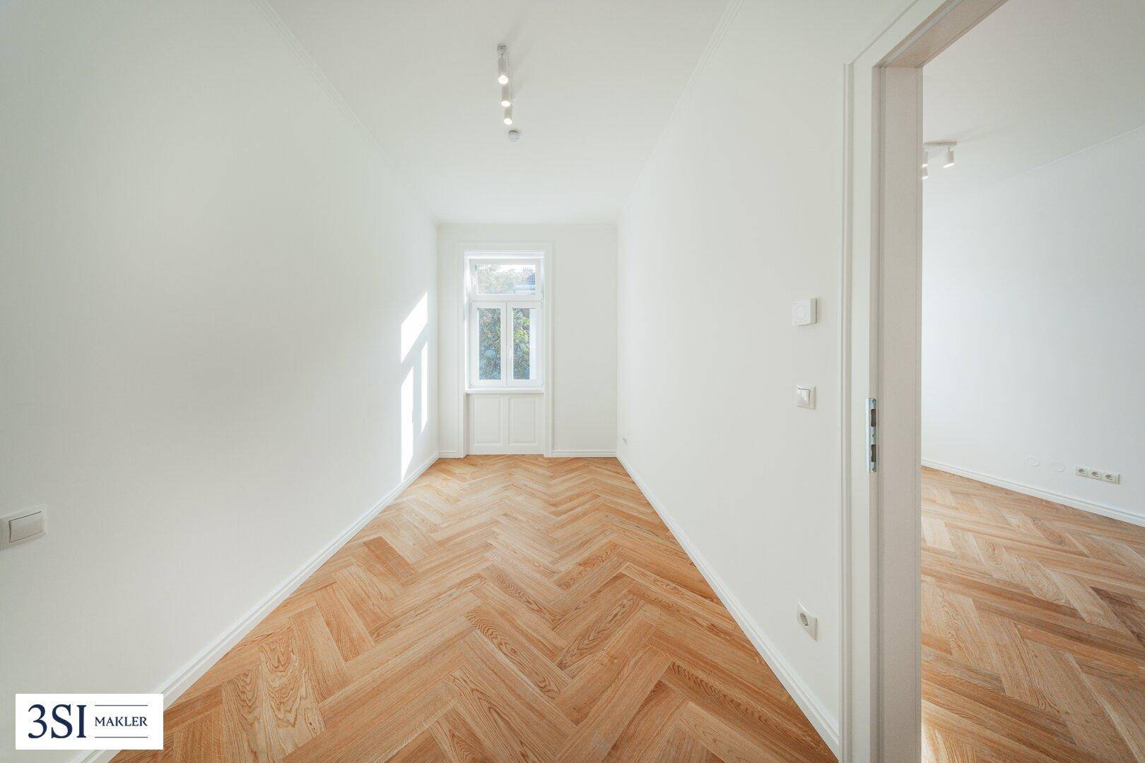 Schmaler, heller Raum mit Fischgrätparkett und einem Fenster, ideal als Arbeitszimmer.