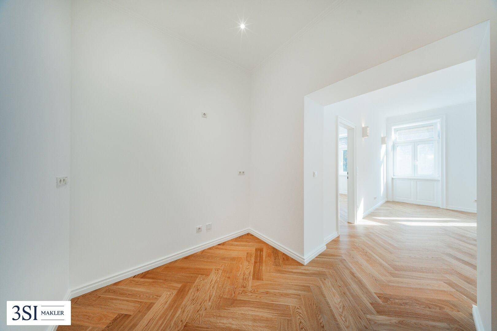 Heller Eckraum mit Fischgrätparkett und Zugang zu einem weiteren Zimmer.