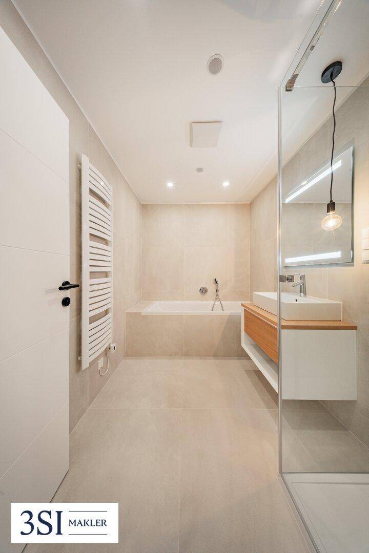 Elegantes Badezimmer mit Badewanne, Glasdusche, modernem Waschtisch und beheiztem Handtuchhalter.
