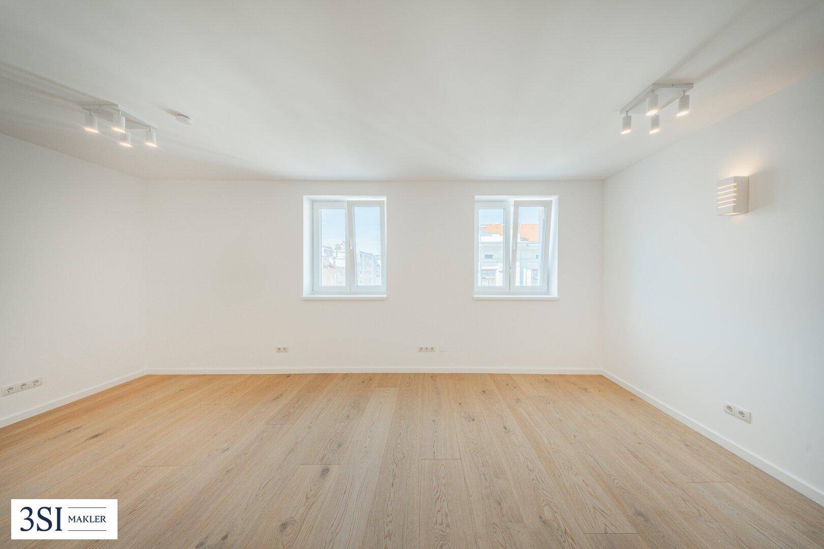 Großer, leerer Raum mit Parkettboden und moderner Deckenbeleuchtung, ideal für flexible Nutzung.
