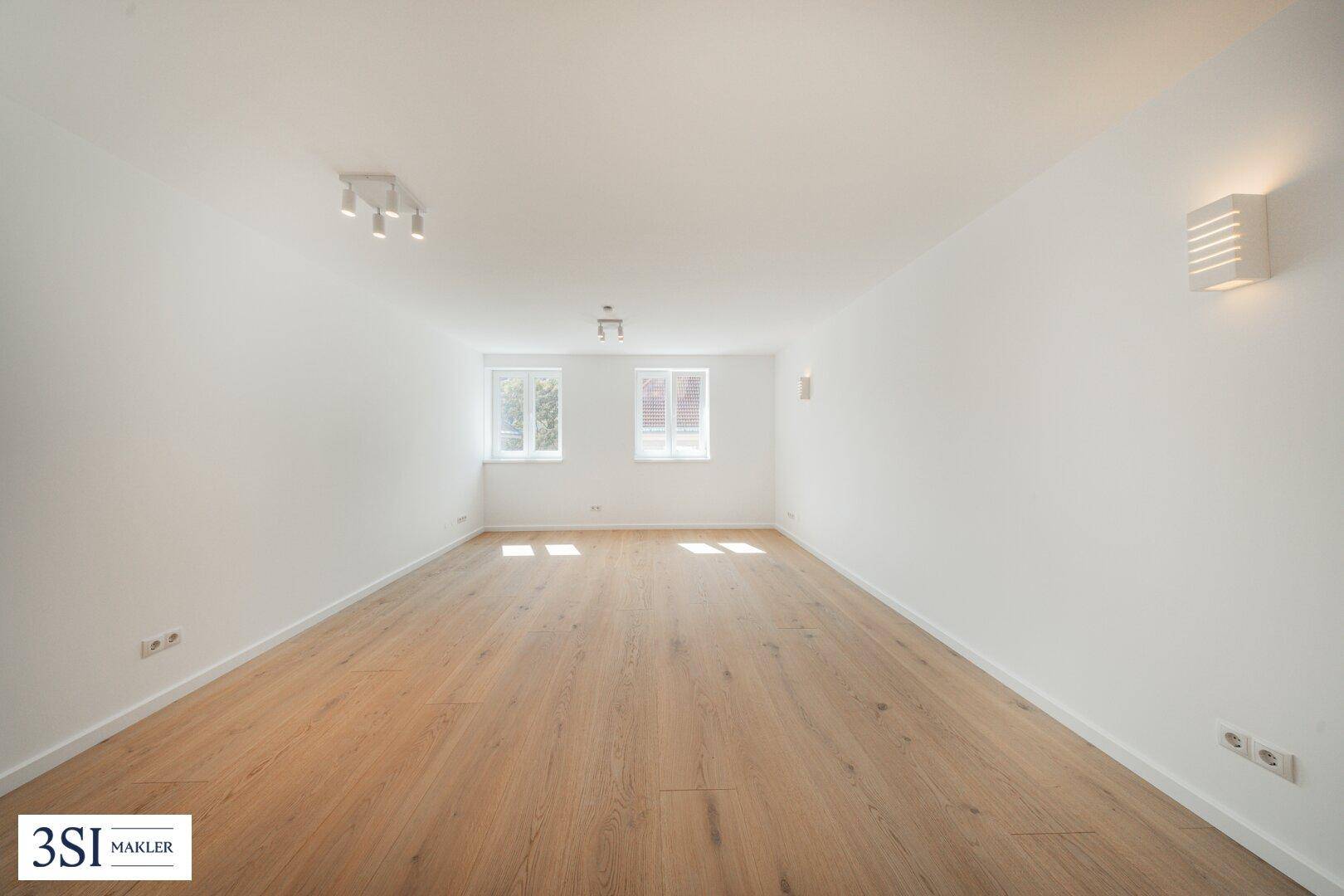 Geräumiges, helles Zimmer mit Holzboden und mehreren Fenstern, ideal als Wohnbereich.