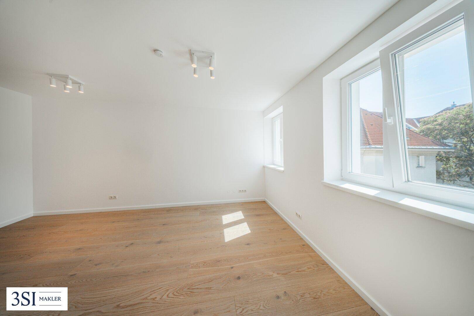 Heller Raum mit Holzboden und großen Fenstern, die viel Sonnenlicht in den Wohnbereich lassen.