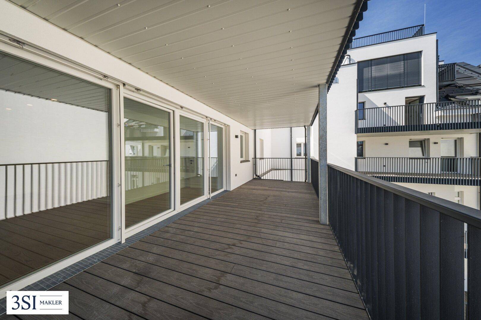 Geräumiger Balkon mit Holzdielenboden, Metallgeländer und Blick auf die umliegenden Gebäude und Bäume.