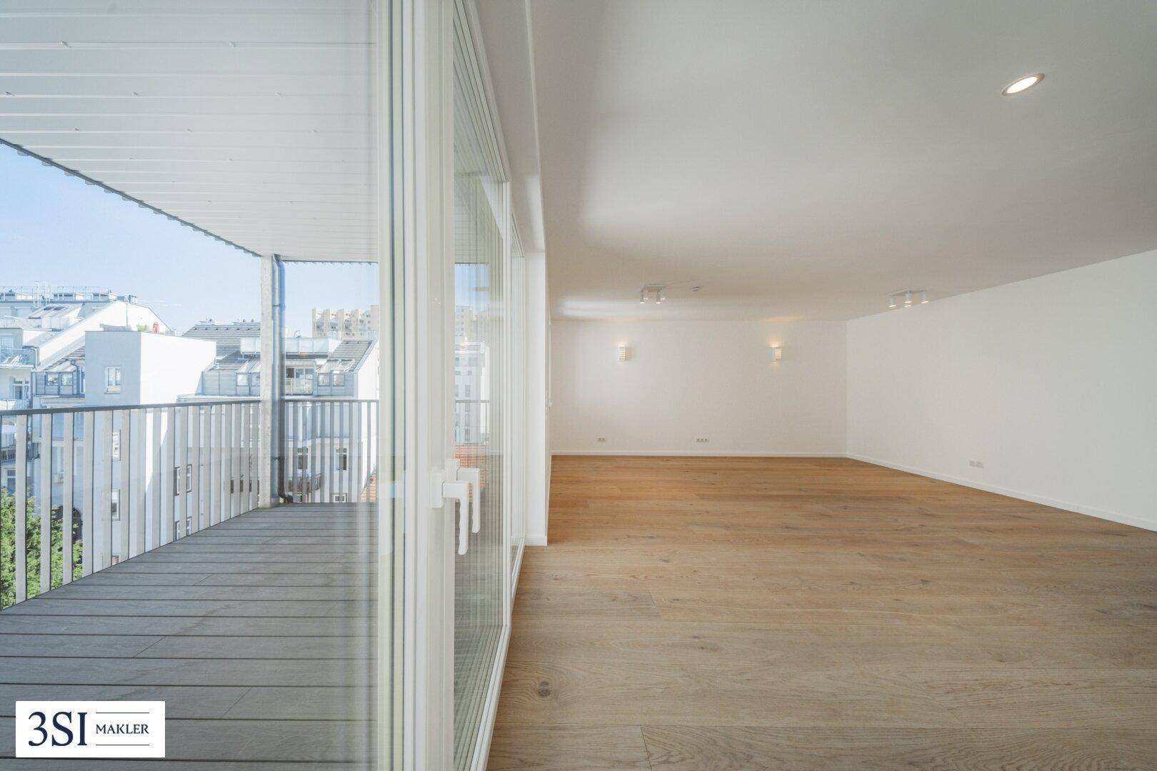 Großzügiger, heller Wohnbereich mit Holzboden und raumhohen Fenstern zum Balkon.