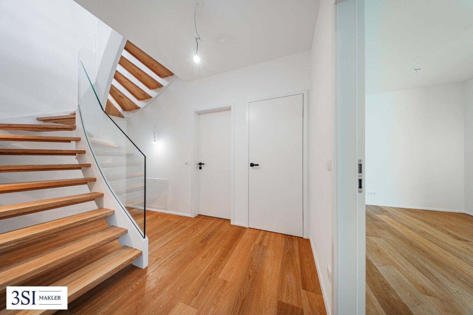 Heller Flur mit eleganter Holztreppe, Glasgeländer und Zugang zu weiteren Räumen.