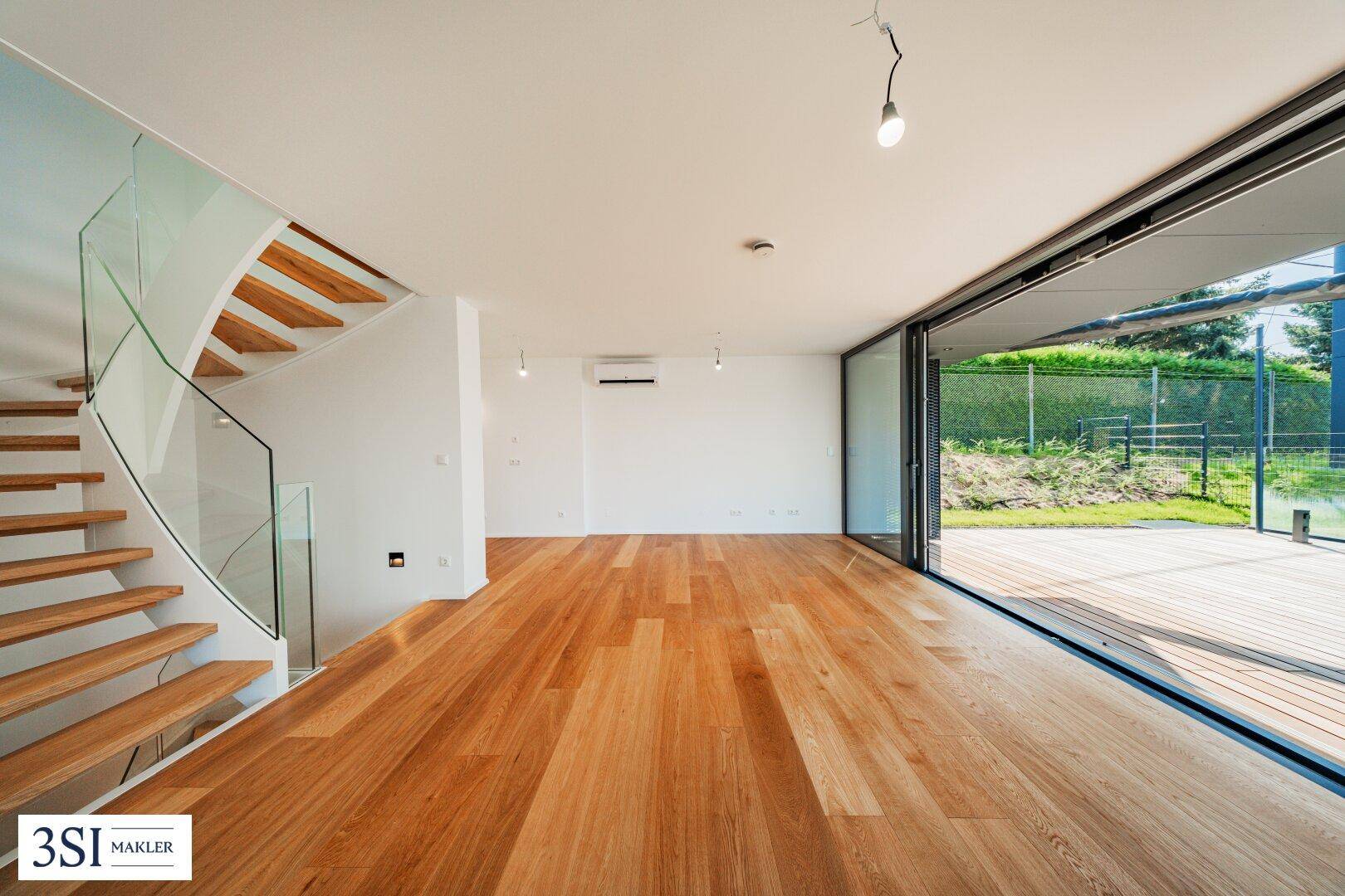 Geräumiger Wohnbereich mit offener Holztreppe, Glasgeländer und Zugang zur Terrasse.
