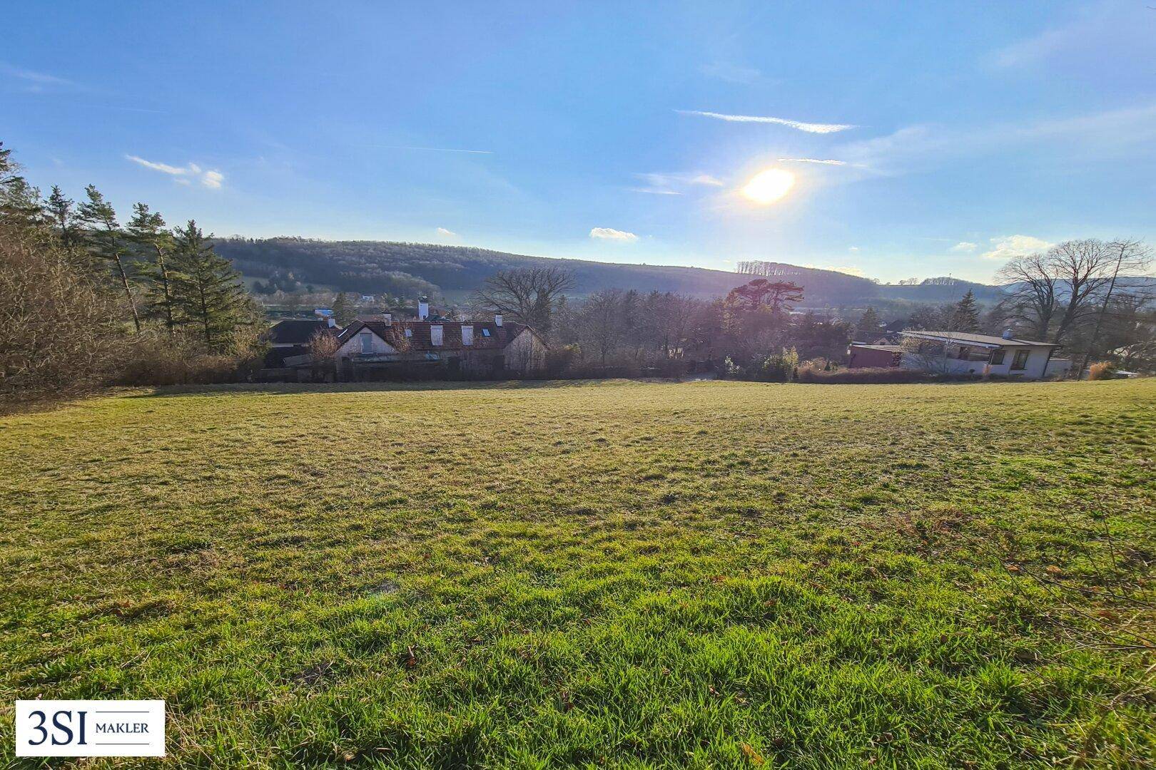 Sonnige Grünfläche mit weitem Blick auf die Umgebung und Häuser im Hintergrund.