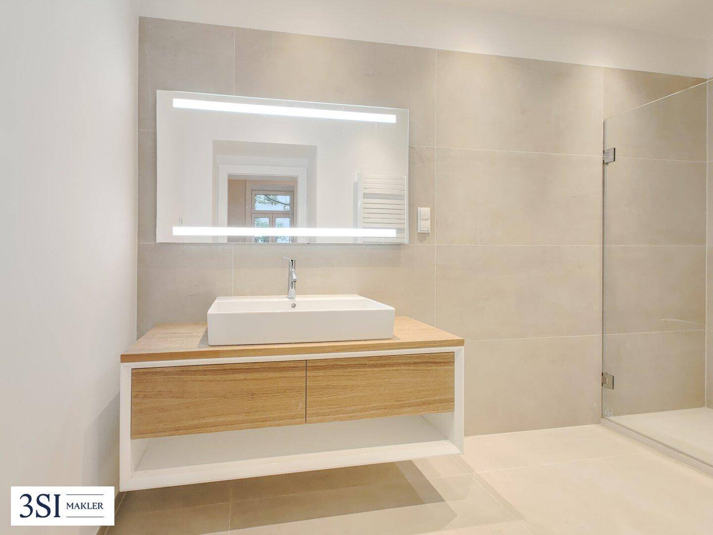 Modernes Badezimmer mit großem Waschtisch, beleuchtetem Spiegel und begehbarer Dusche.