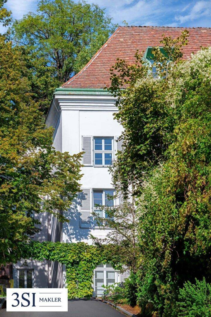 Detailansicht der historischen Fassade mit Fensterläden, umgeben von dichtem Grün und Bäumen.