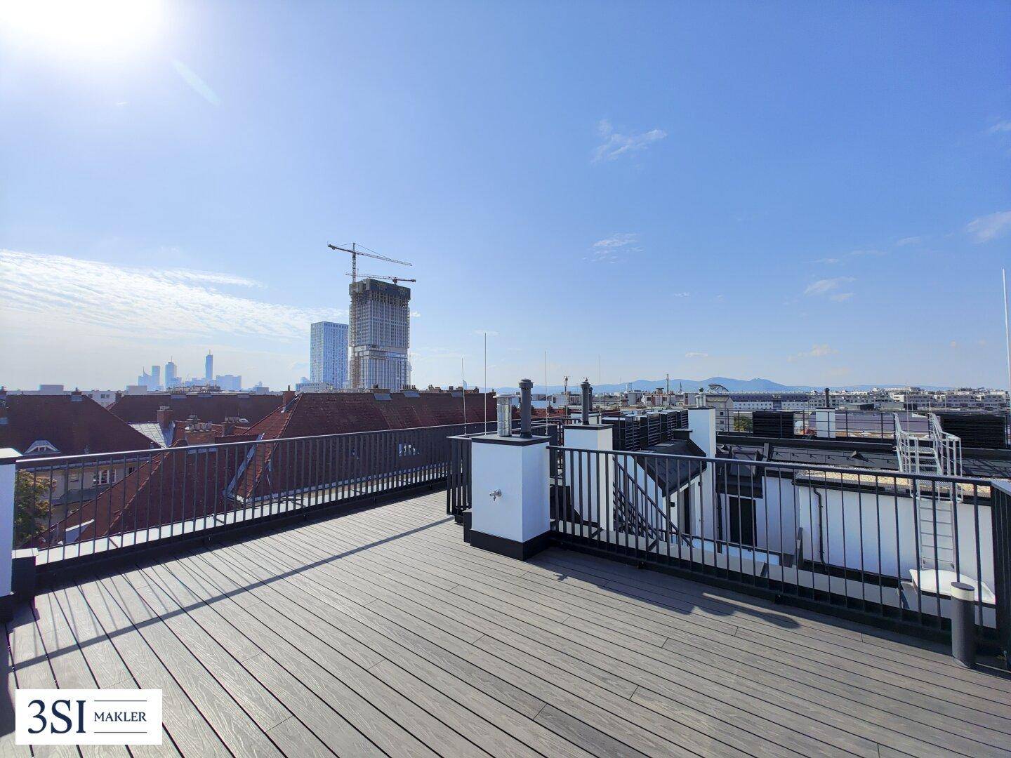 Geräumige Dachterrasse mit Holzboden und Panoramablick über die Stadt und umliegende Gebäude.