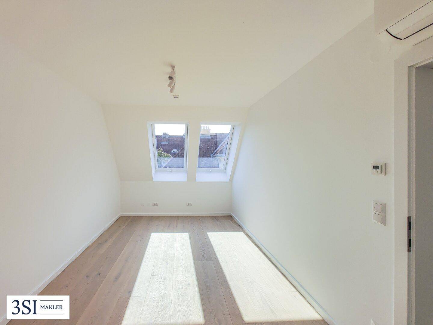 Helles Schlafzimmer im Dachgeschoss mit Holzboden, weißen Wänden und zwei Dachfenstern.