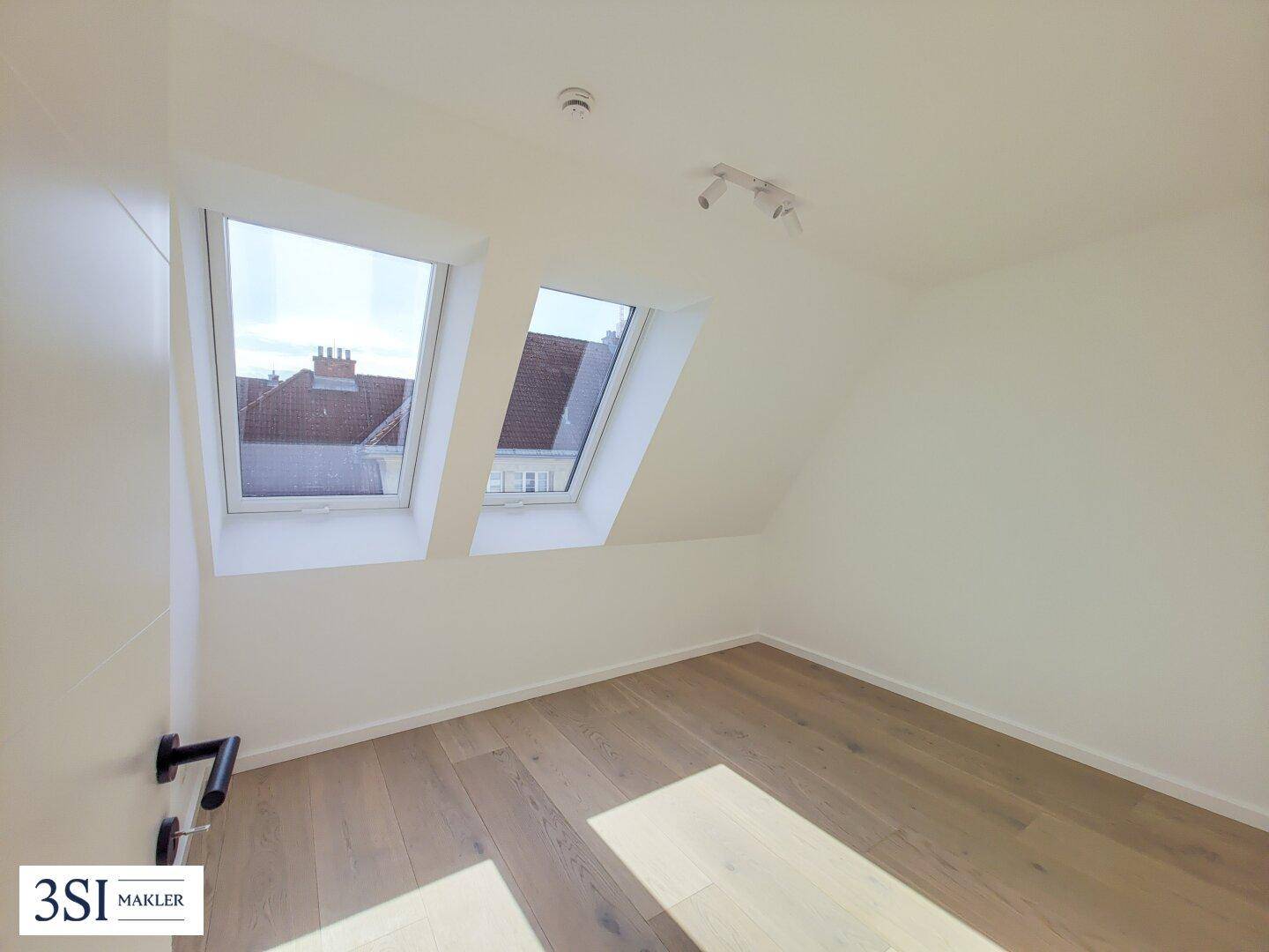 Gemütliches Schlafzimmer im Dachgeschoss mit Holzboden, weißen Wänden und zwei Dachfenstern.