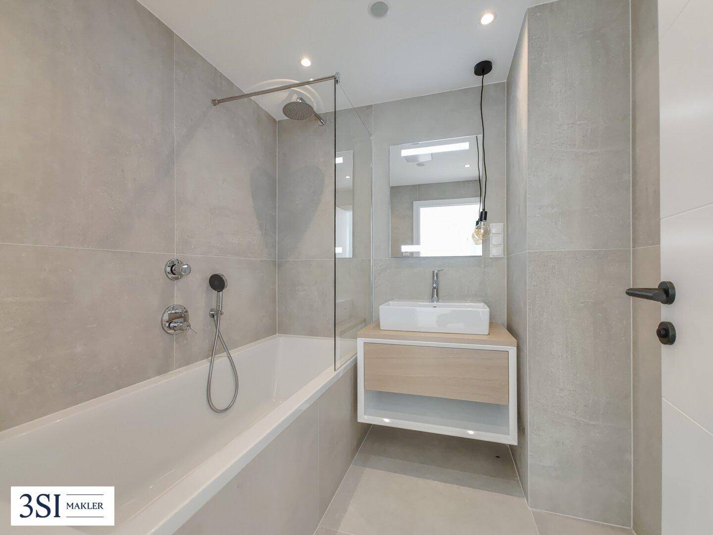 Modernes Badezimmer mit grauen Fliesen, Badewanne, Regendusche und elegantem Waschtisch.