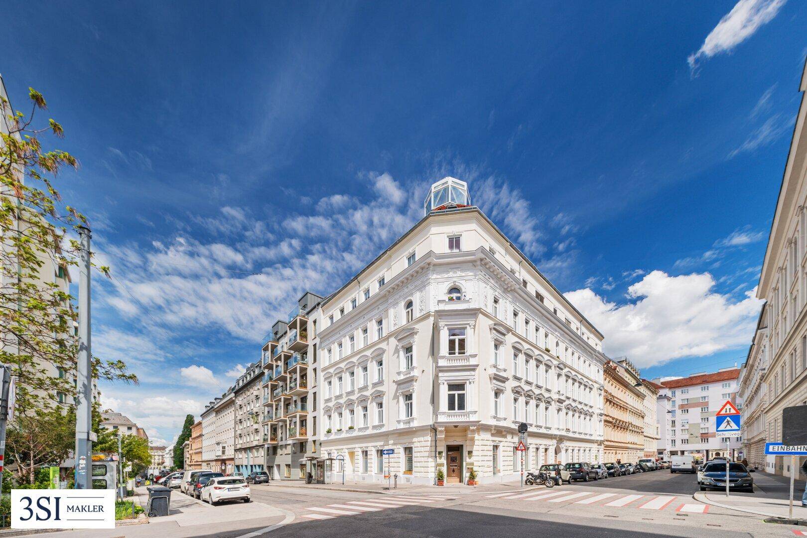 Elegantes Eckgebäude mit klassischer Architektur und weißer Fassade unter blauem Himmel in städtischer Umgebung.