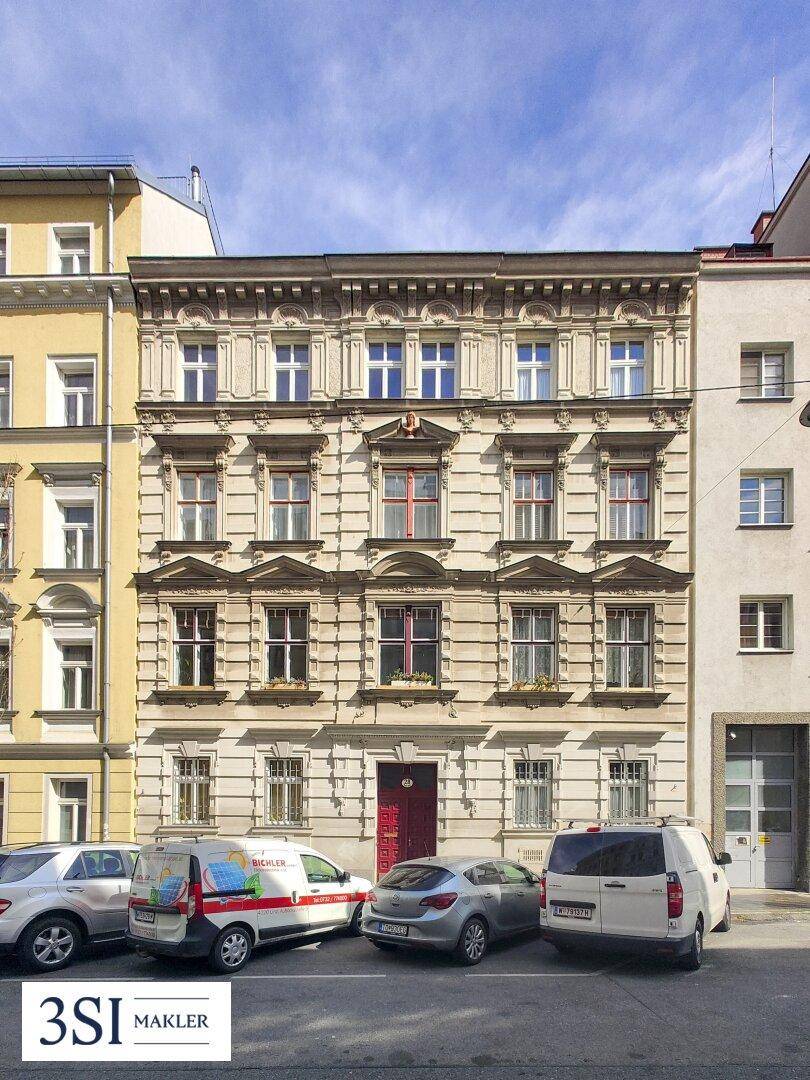 Historisches Mehrfamilienhaus mit klassischer Fassade und geparkten Autos davor.