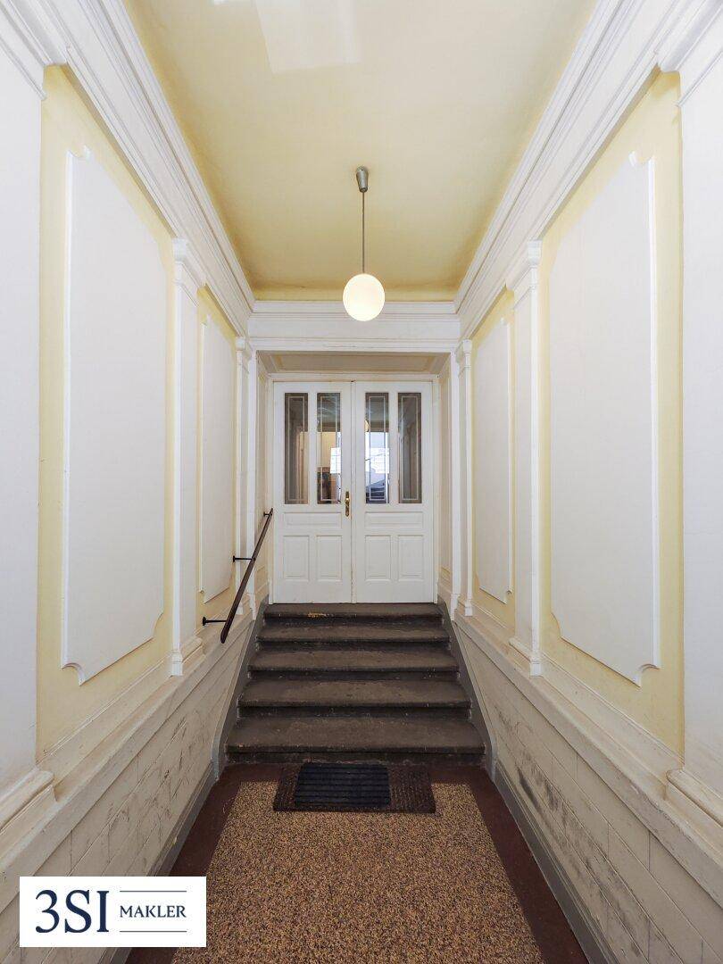 Historisches Treppenhaus mit Terrazzoboden, Stuckelementen und klassischer Eingangstür.