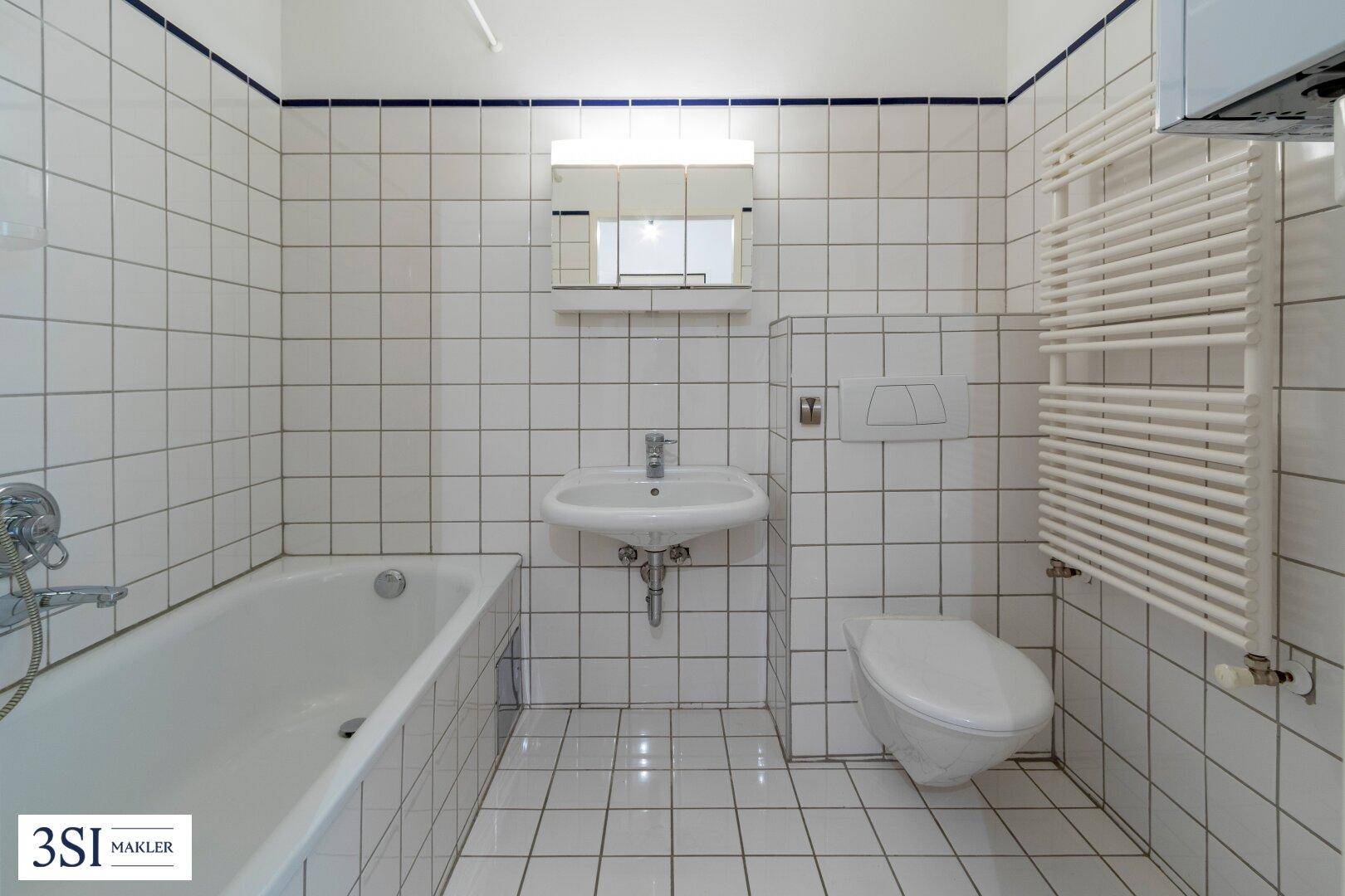 Helles Badezimmer mit weißen Fliesen, Badewanne, WC und Handtuchheizkörper.