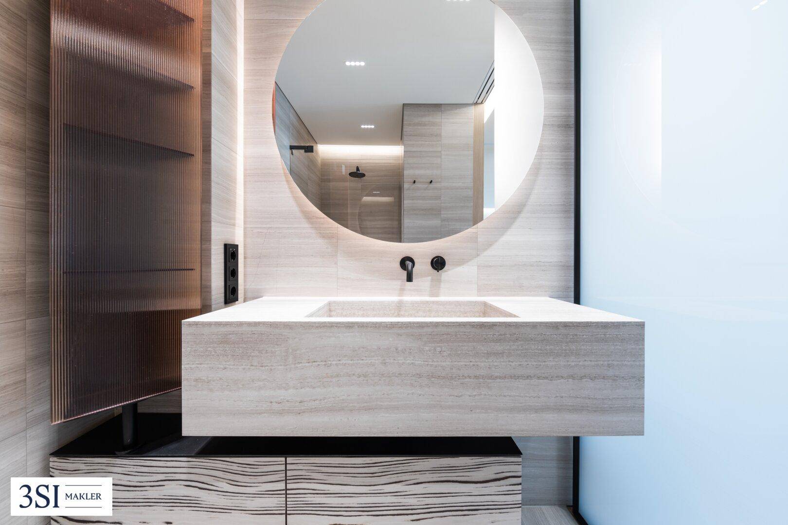 Elegantes Badezimmer mit schwebendem Waschtisch, rundem Spiegel und modernen Armaturen.