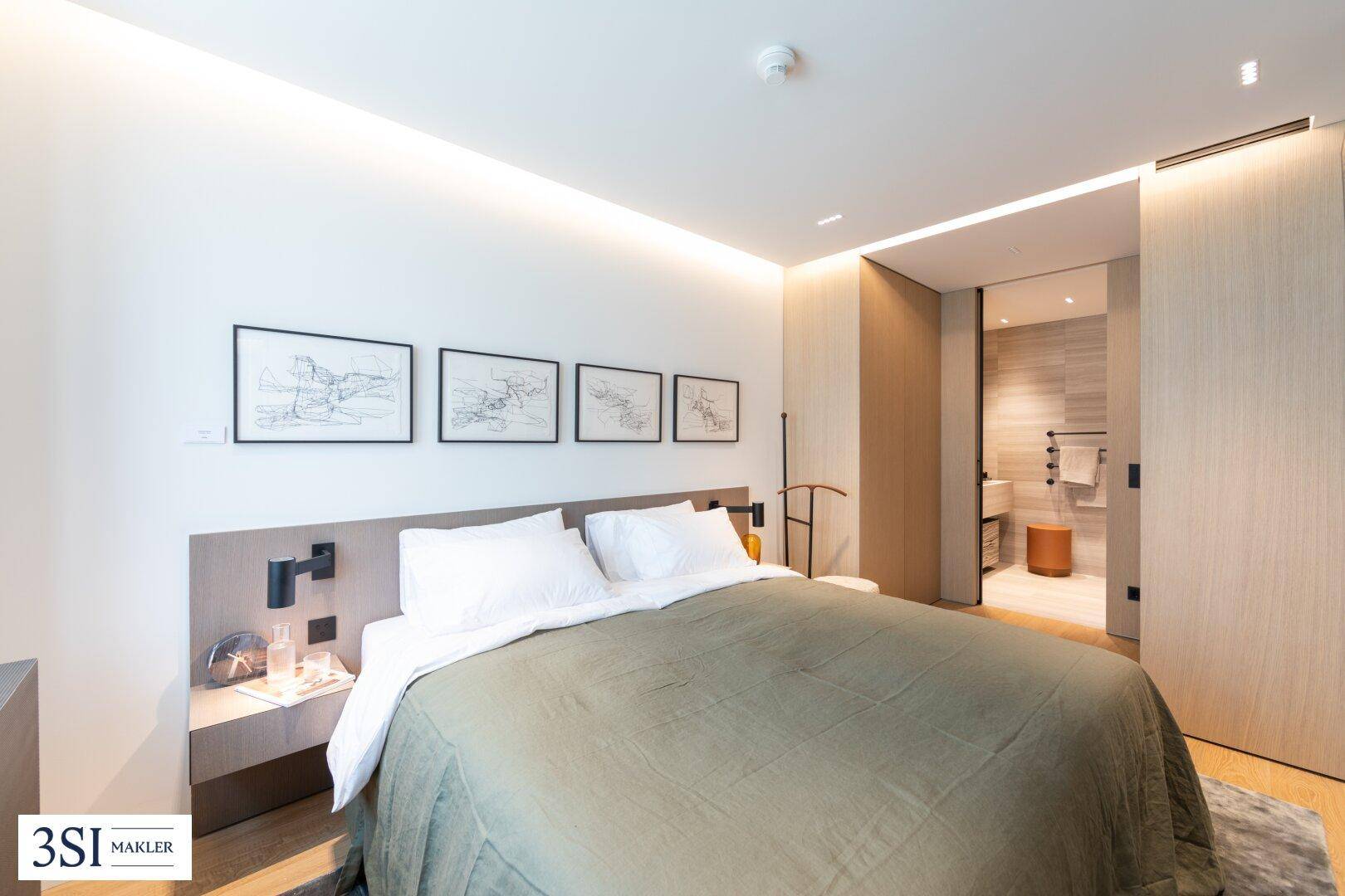 Helles Schlafzimmer mit großem Bett, Holzboden und direktem Zugang zu einem modernen Badezimmer.
