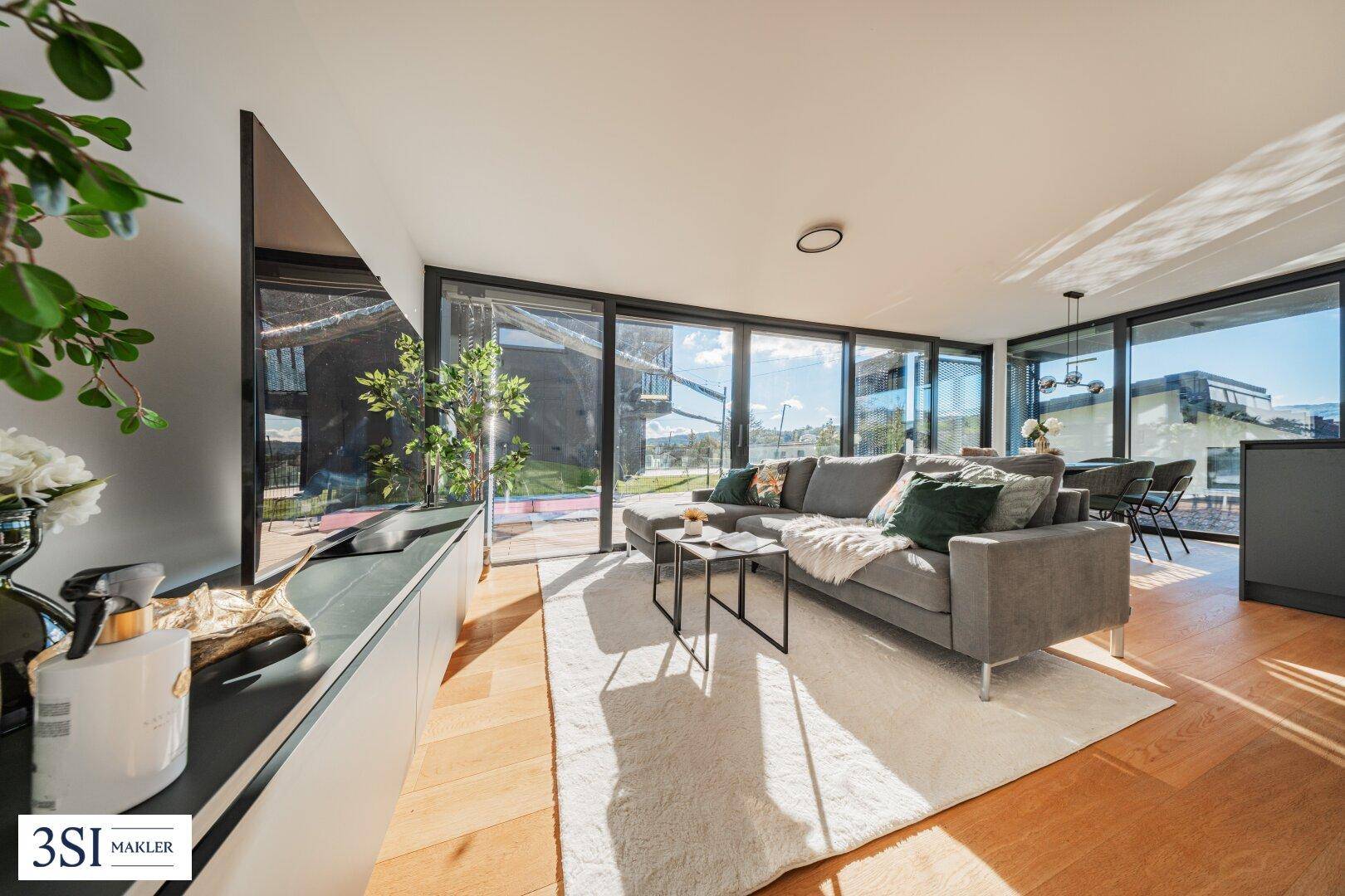 Geräumiger Wohnbereich mit bequemer Couch, Holzboden und Zugang zu großen Fensterfronten.