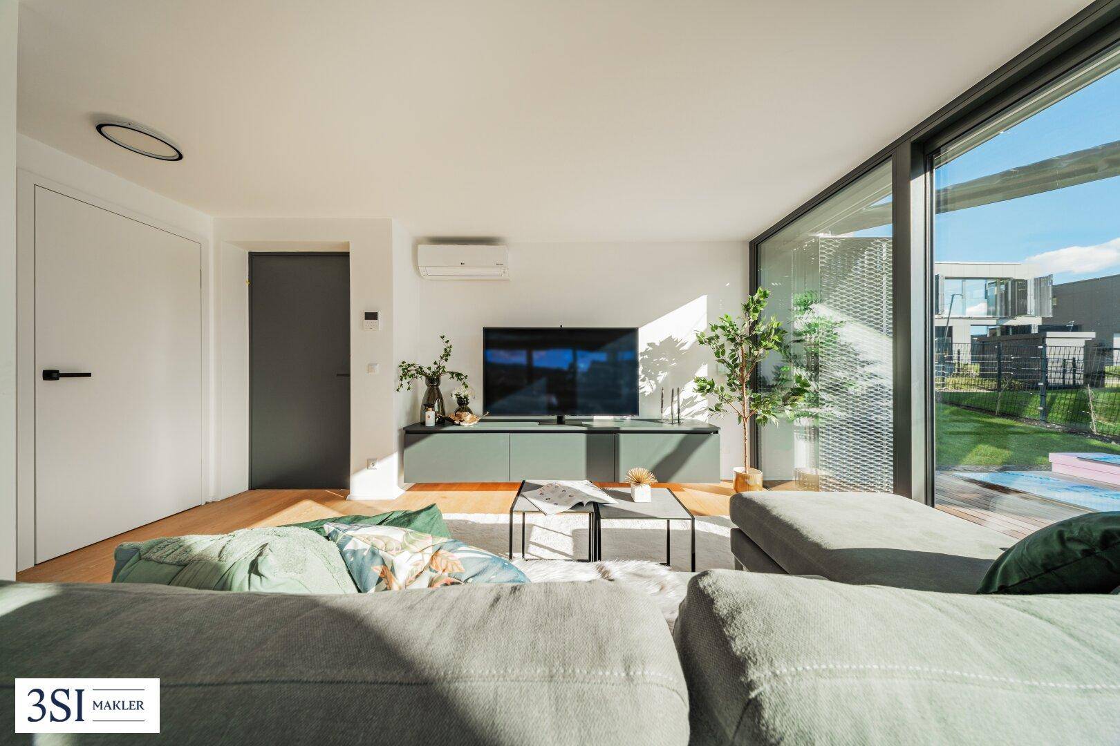 Helles Wohnzimmer mit großen Fensterfronten, Holzboden und modernem Sofa.