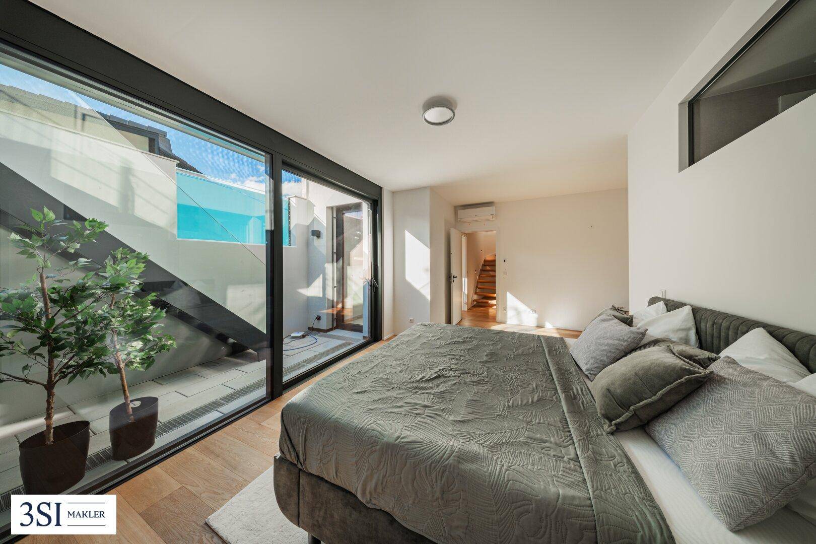 Schlafzimmer mit großen Fensterfronten, Holzboden und Zugang zu einem Außenbereich.