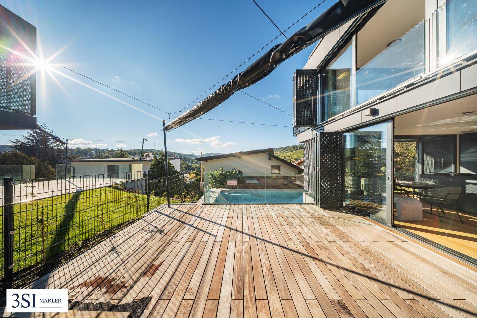 Geräumige Holzterrasse mit Metallzaun und Blick auf den Pool und die Umgebung.