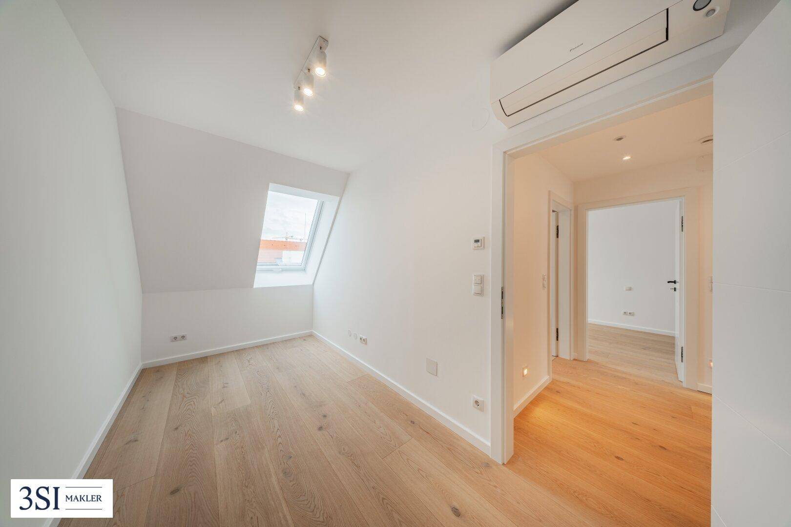 Helles Schlafzimmer im Dachgeschoss mit Holzboden, Dachfenster und Klimaanlage.