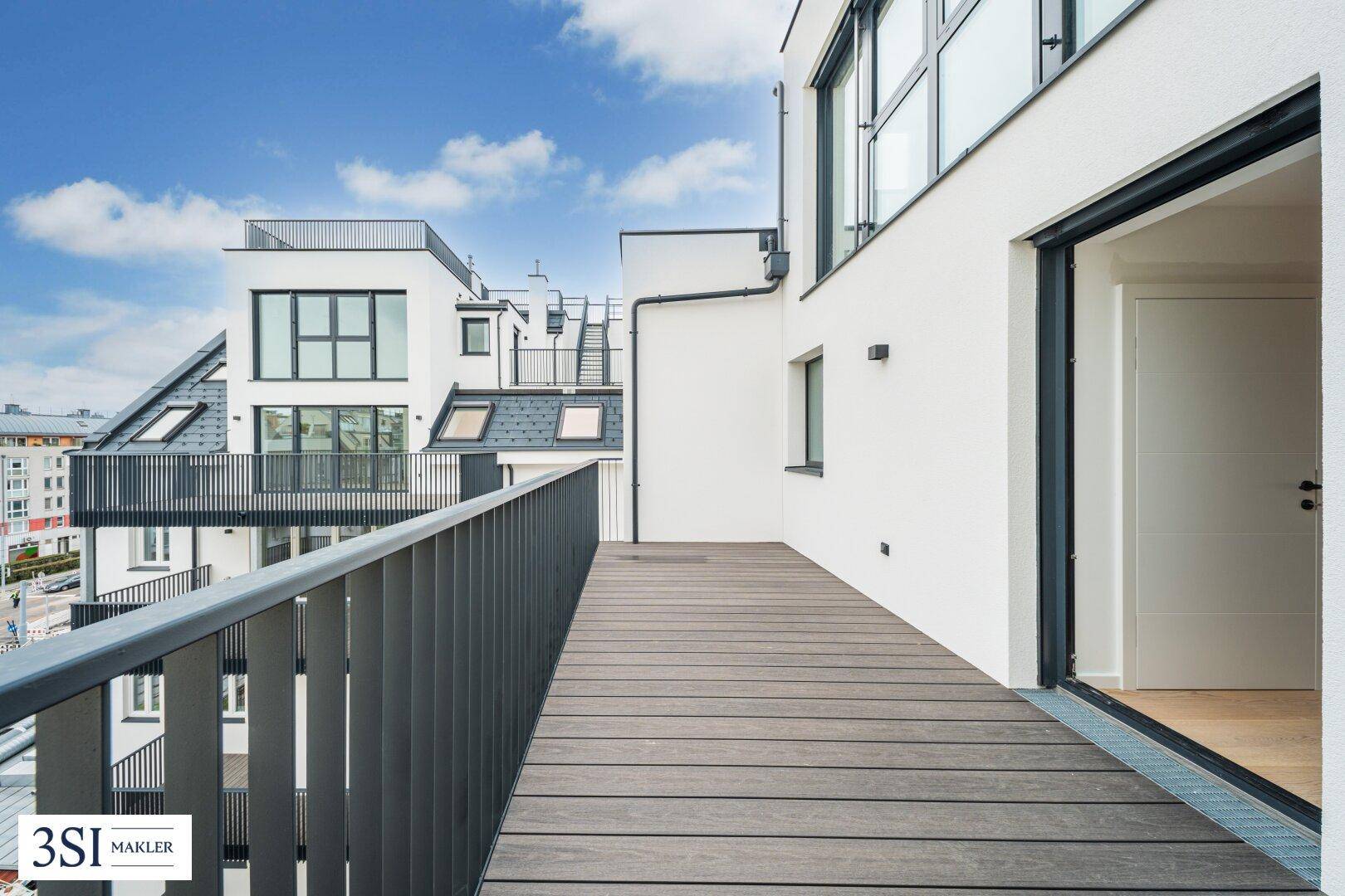 Geräumige Terrasse mit Holzdielenboden, modernem Geländer und Blick auf umliegende Gebäude.