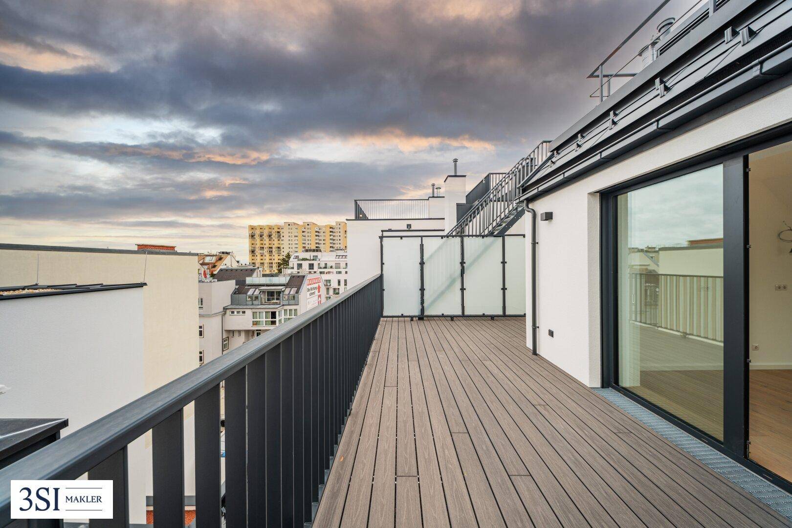 Langer Balkon mit Holzboden und Glasgeländer, bietet weiten Blick über die Stadtlandschaft.