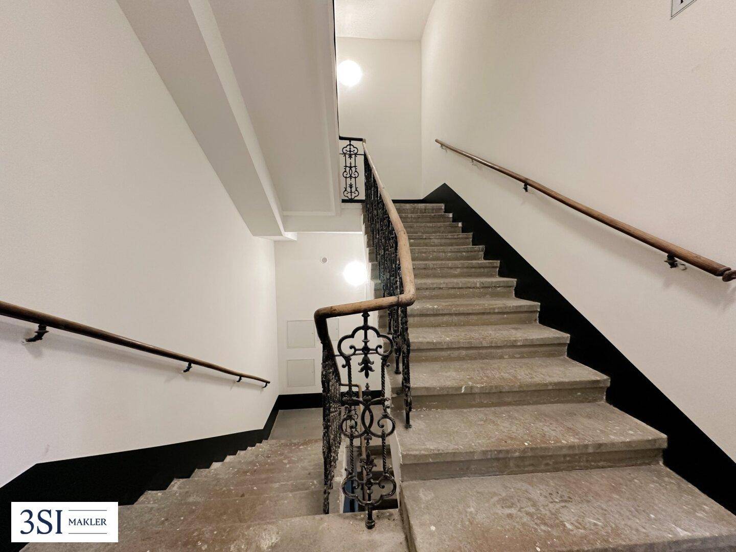 Historisches Treppenhaus mit Steinstufen, schmiedeeisernem Geländer und Holzhandläufen.